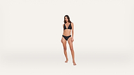 A woman stands barefoot against a plain white background, wearing a black bikini.