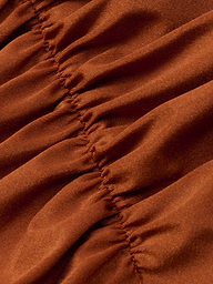 A close-up of the Lilou One-Piece Swimsuit in rust shows gathered fabric with visible vertical stitching that creates soft folds and textured, ruched lines. The material looks smooth and slightly shiny, highlighting the high-leg cut design.