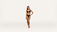 A woman stands barefoot against a plain white background, wearing a black bikini. She has long hair and her right hand rests on her hip.