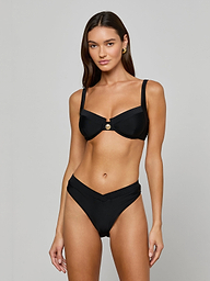 Woman wearing the Ashleigh Bikini Bottom, a black V-cut bikini with Trapunto stitching, paired with an underwire top featuring a central gold button, standing against a plain off-white background.