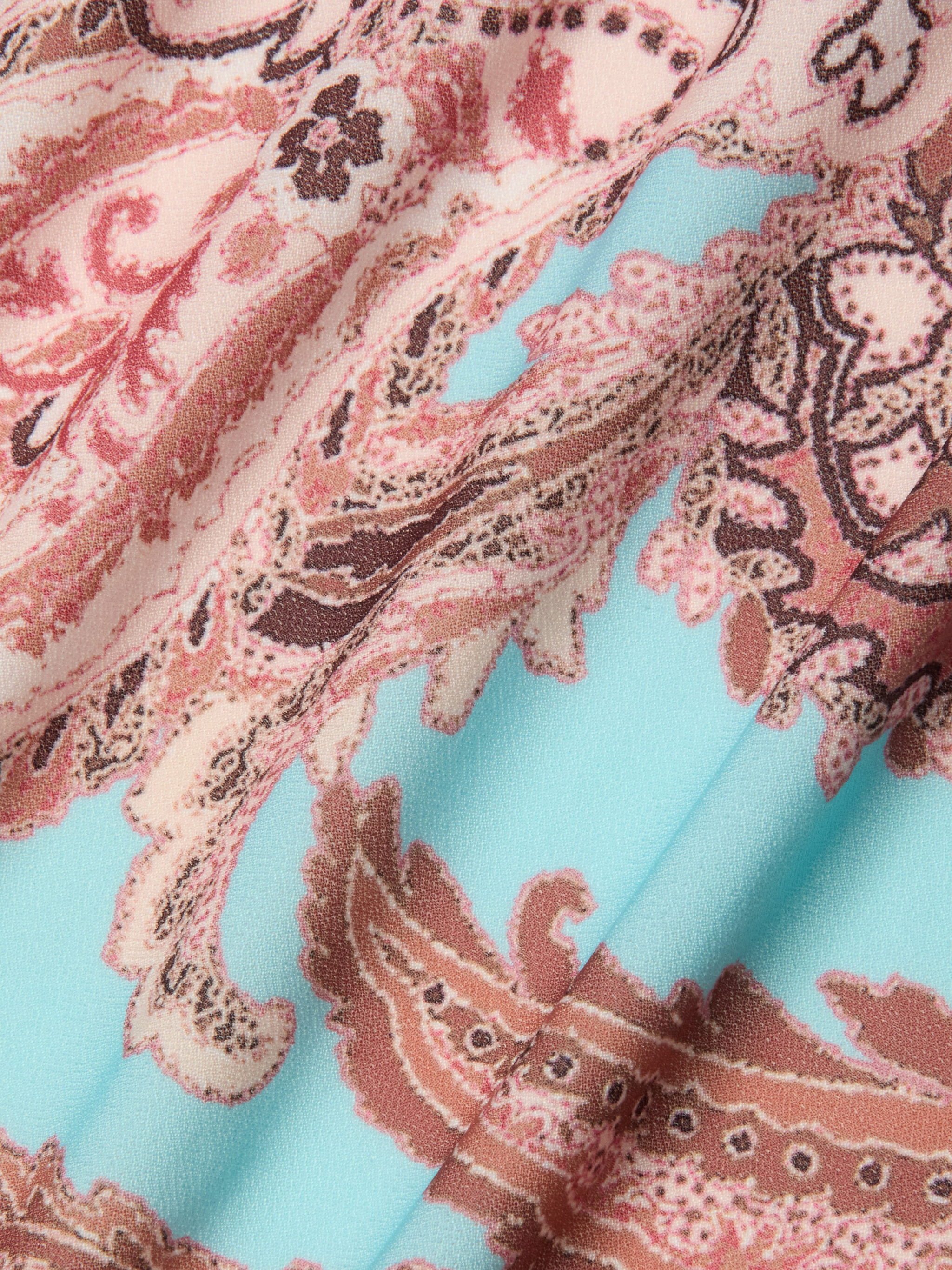 Close-up of the fabric used in the Marena Sarong, featuring a paisley pattern in shades of pink, brown, and cream set against a light blue background. The material looks soft and slightly textured with gentle folds and shadows, making it an ideal choice for a stylish swimwear cover-up that adds beachside sophistication to any ensemble.