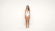 A woman stands facing forward against a plain white background, wearing a white one-piece swimsuit with black trim.