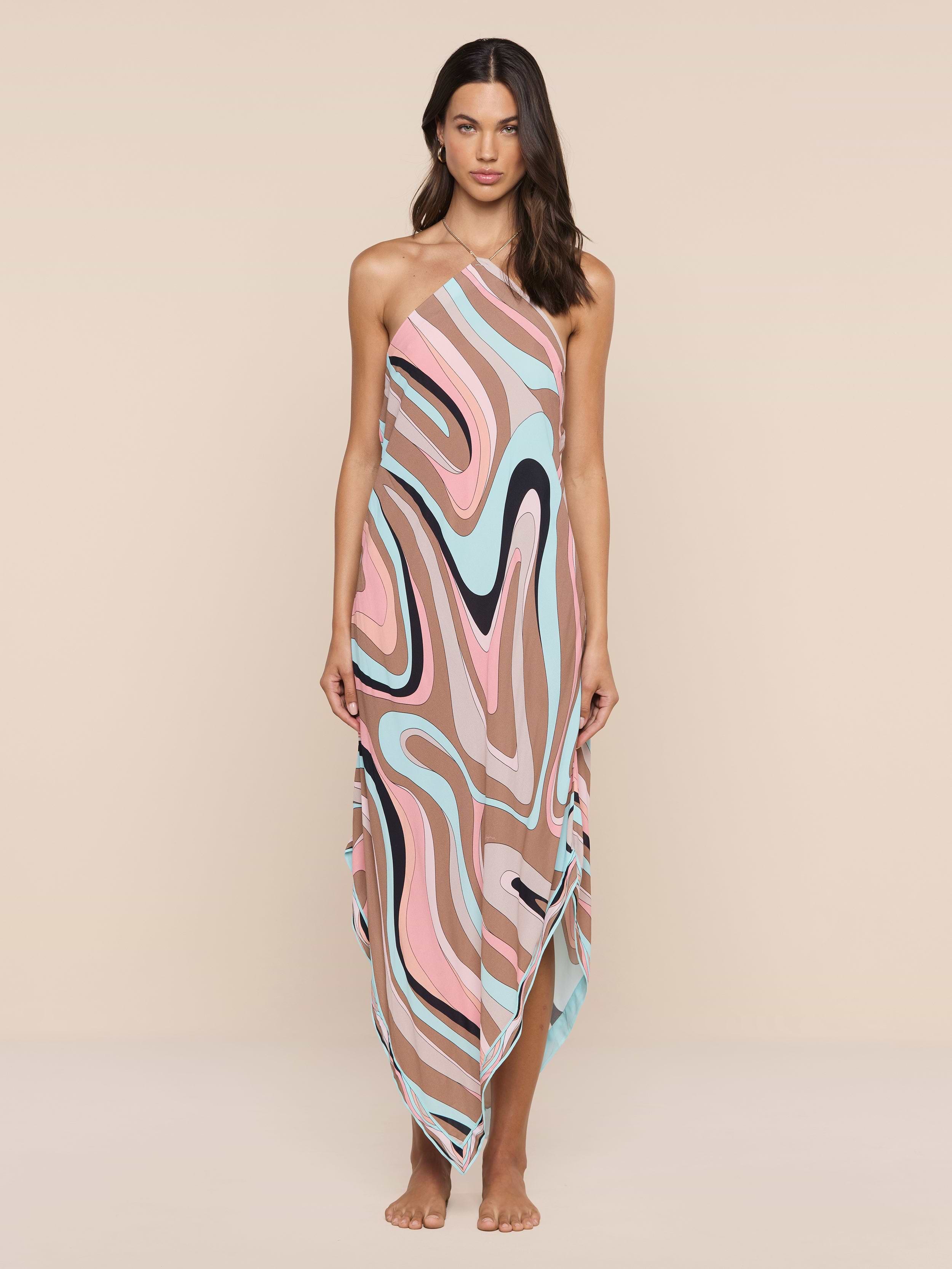 Eine Frau steht barfuß vor einem beigen Hintergrund und trägt das Elise Cover-Up Dress - ein Halfter-Midikleid mit abstraktem Wirbeldruck, ärmellosem Design, fließendem Taschentuch-Saum und asymmetrischem Nackenband für einen mühelosen, modernen Stil.