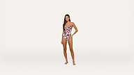 Woman stands barefoot in a floral one-piece swimsuit against a plain white background, facing forward with one hand on her hip.