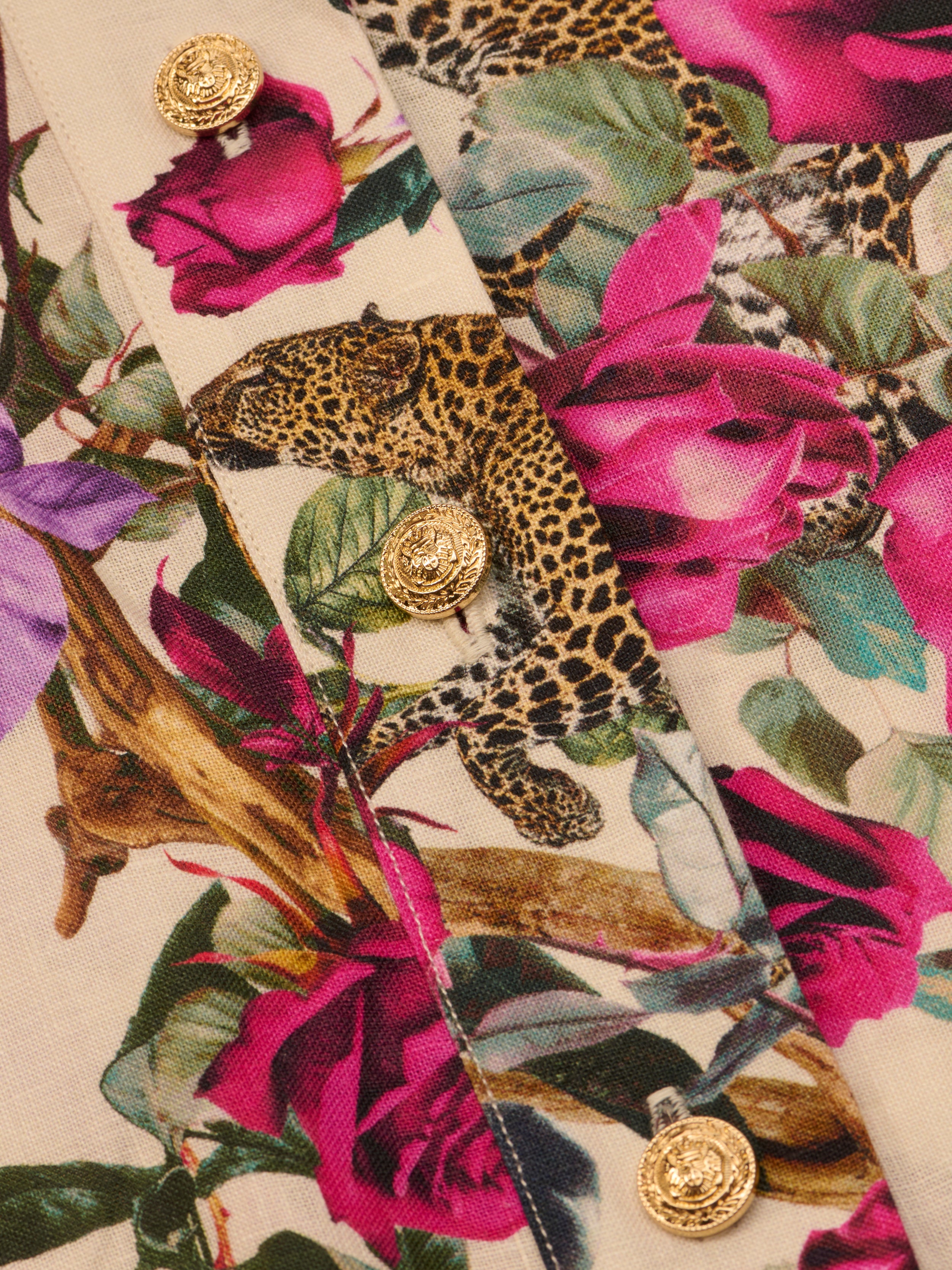 Close-up of the Hestia Cover-Up Romper’s rose leopard print fabric, featuring pink flowers and gold decorative buttons sewn onto the material.