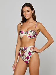 A woman poses in the Alexandria Bikini Top, a white balconette style with rose leopard print featuring underwire and adjustable straps. She pairs it with matching high-waisted bottoms, standing against a plain light background.