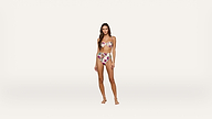 A woman stands on a plain white background, wearing a floral bandeau bikini top and high-waisted bikini bottoms. She has long brown hair and is barefoot, facing forward with a relaxed expression.