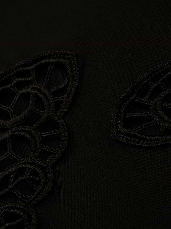 Close-up of the Remi One-Piece Swimsuit’s black fabric, featuring geometric, lace-like embroidered patterns reminiscent of poolside glamour. The textured embroidery creates a subtle contrast against the smooth background.