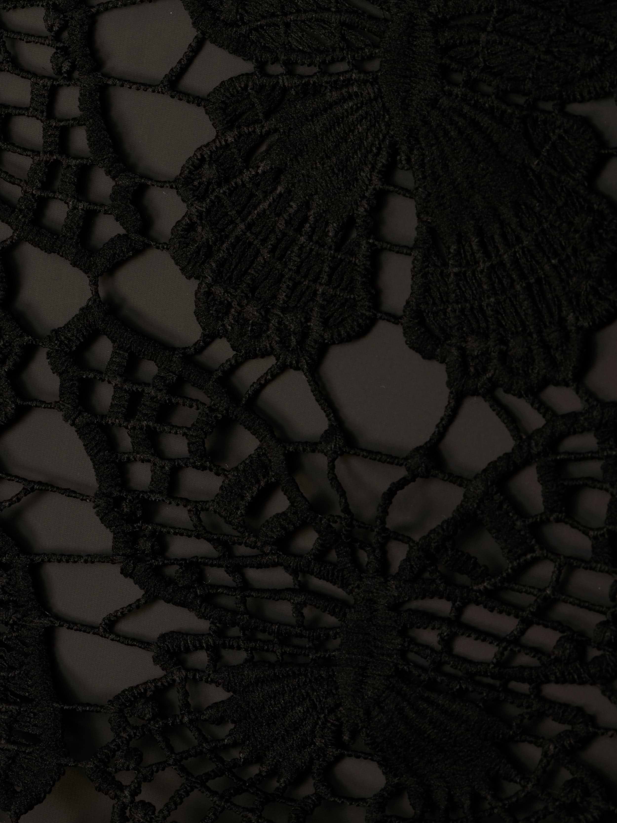 Close-up of the Janus Cover-Up Robe in black lace fabric, showcasing an intricate butterfly crochet pattern with delicate threads forming detailed wings and a finely textured appearance.