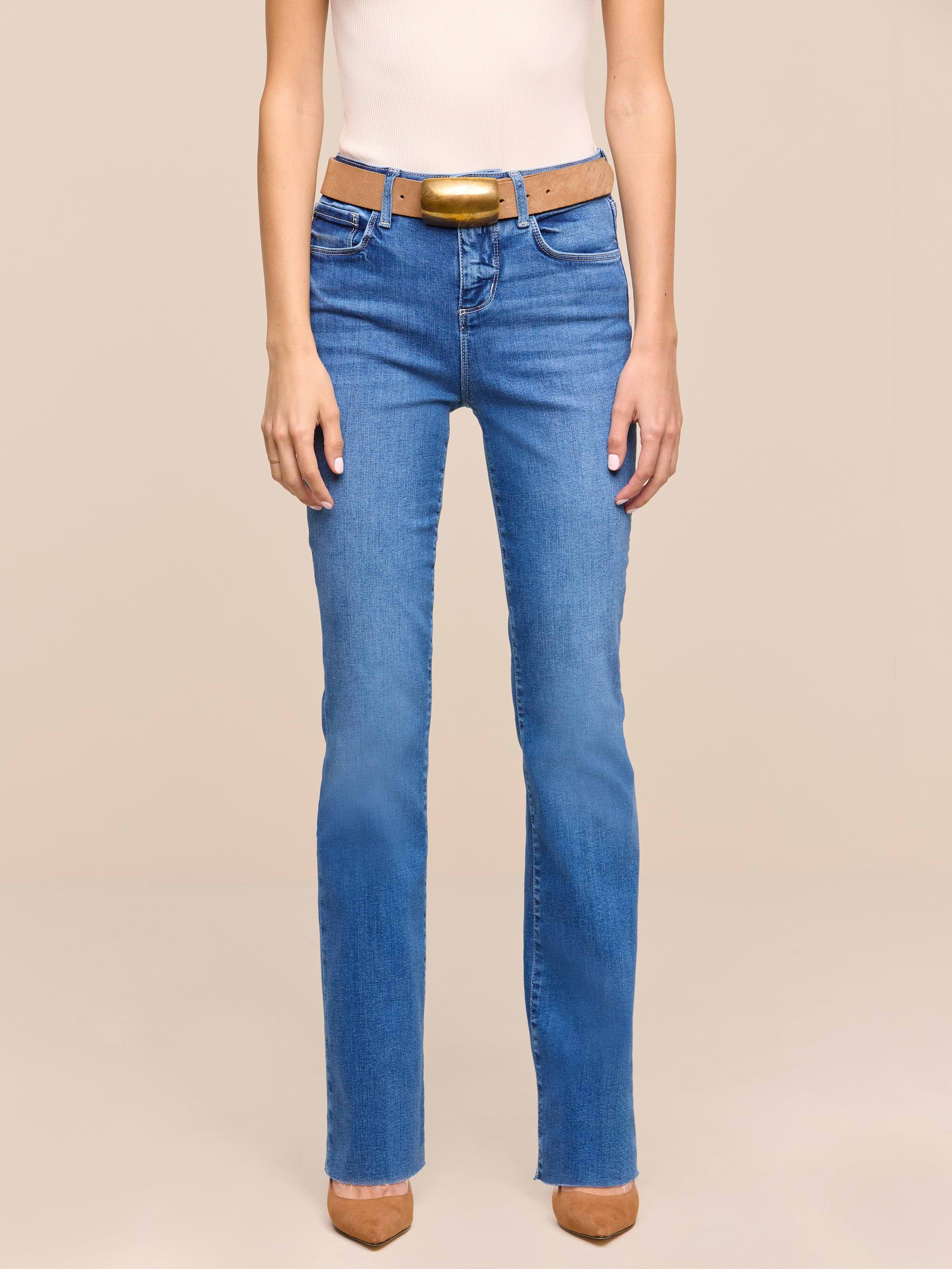 A person is shown from the shoulders down, wearing a sleeveless beige top, a brown belt, brown pointed-toe shoes, and heritage indigo wash Petite Ruth Straight-Leg Jean, standing against a plain white background.