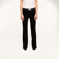 A person wearing a white sleeveless top, the Petite Stevie Velvet Jean with a belt, and black pointed shoes stands against a plain white background, facing forward.