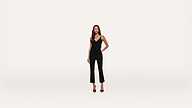 A woman wearing a black sleeveless top, black pants, and black heels stands against a plain white background.