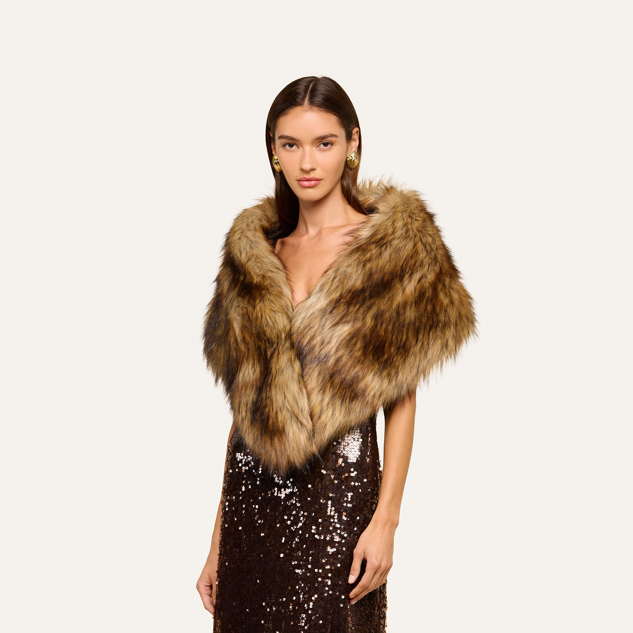 Wearing the Hazel Faux Fur Stole as a statement accessory over her shoulders, a woman in a brown sequin dress stands against a plain, light background, radiating plush glamour.