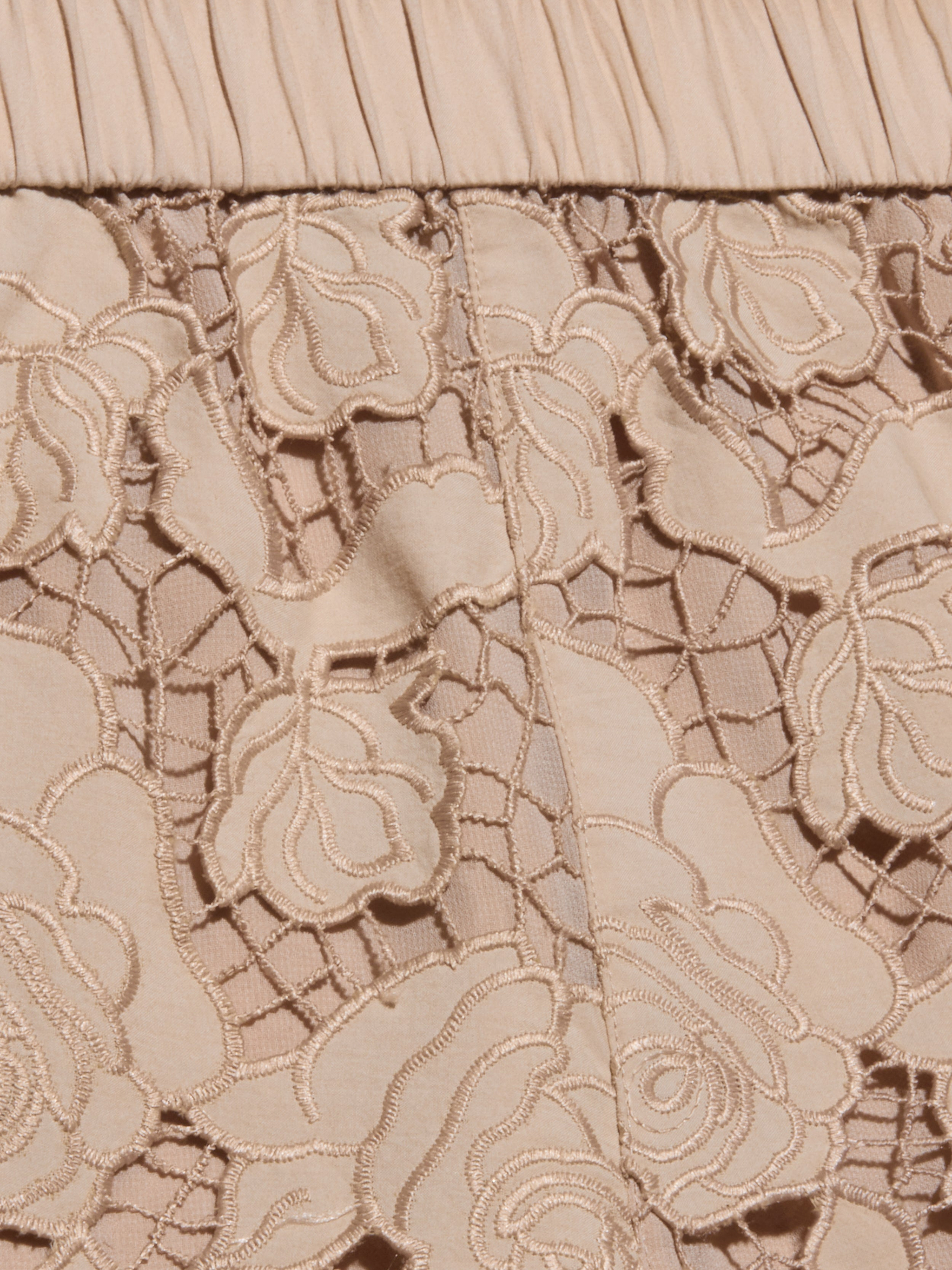 Close-up of almond tan fabric with floral lace embroidery and pleated detailing at the top edge. The lace features intricate flower patterns over a solid background, reminiscent of the delicate design found in the Laina Eyelet Short.