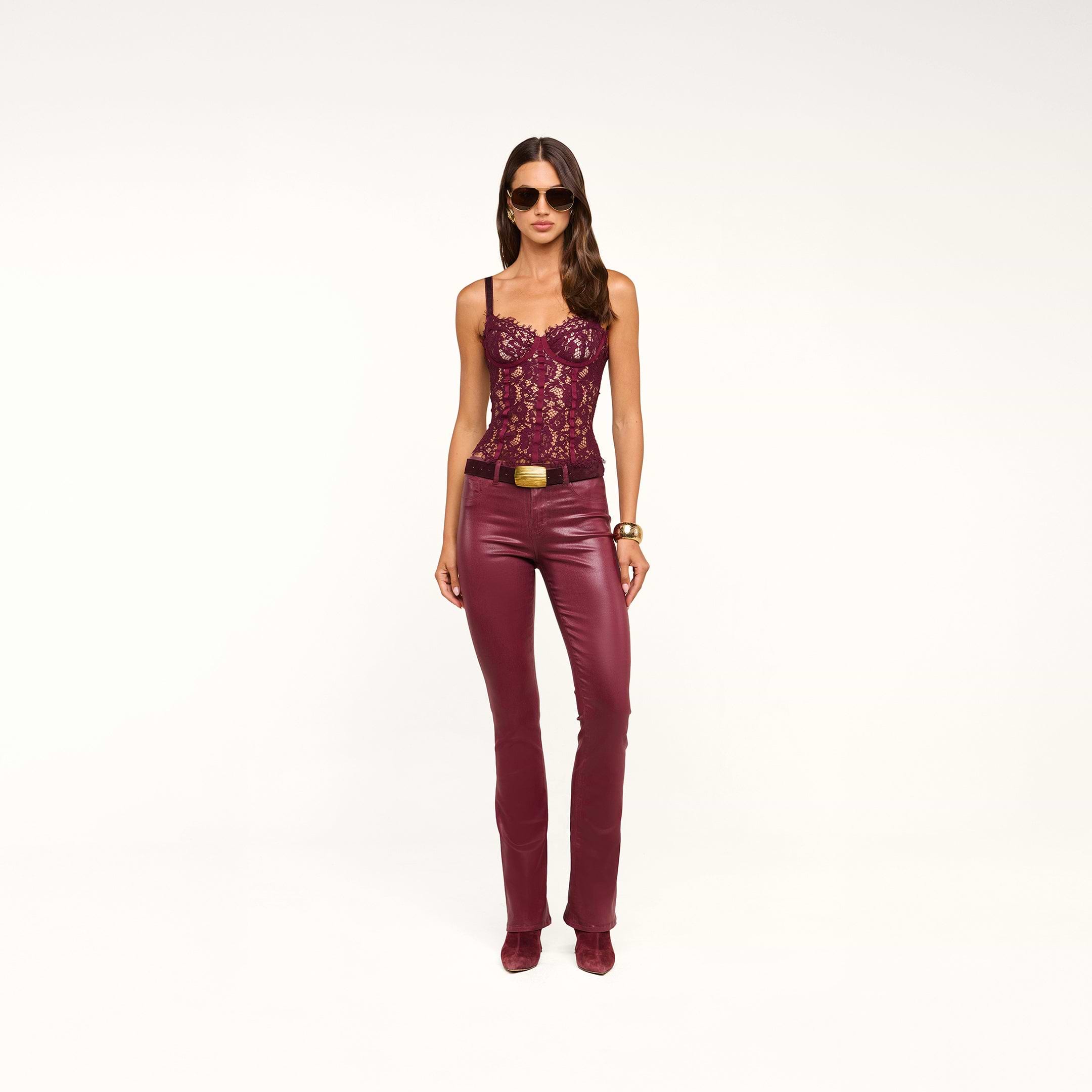 A woman wearing sunglasses, a burgundy lace top, and the Selma Coated Bootcut Jean stands against a plain white background.