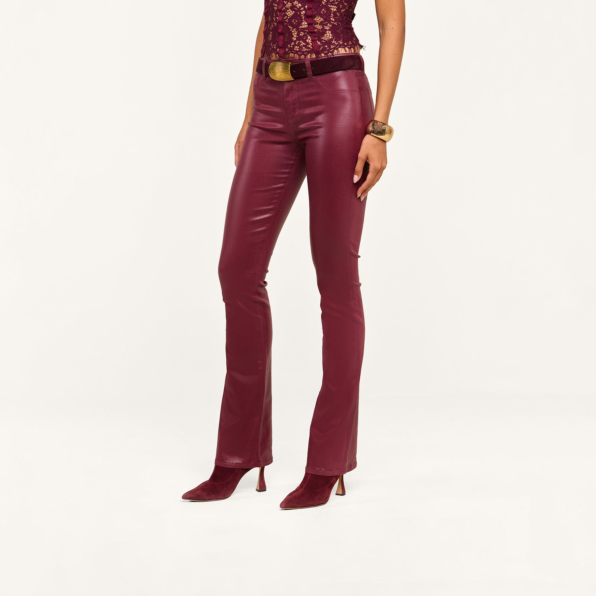 Wearing the Selma Coated Bootcut Jean in a maroon leather-alternative finish, paired with matching pointed-toe boots, a lace top, a brown belt with a gold buckle, and a chunky bracelet. The photo is cropped from the shoulders down.