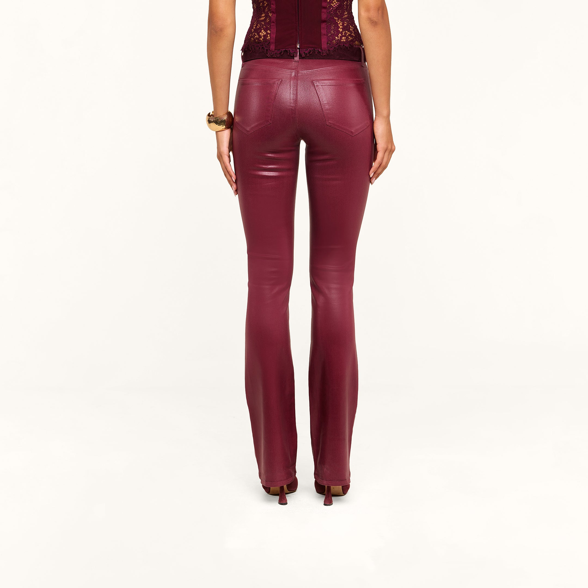 A person wearing the Selma Coated Bootcut Jean in maroon with high heels is standing with their back to the camera against a plain white background.