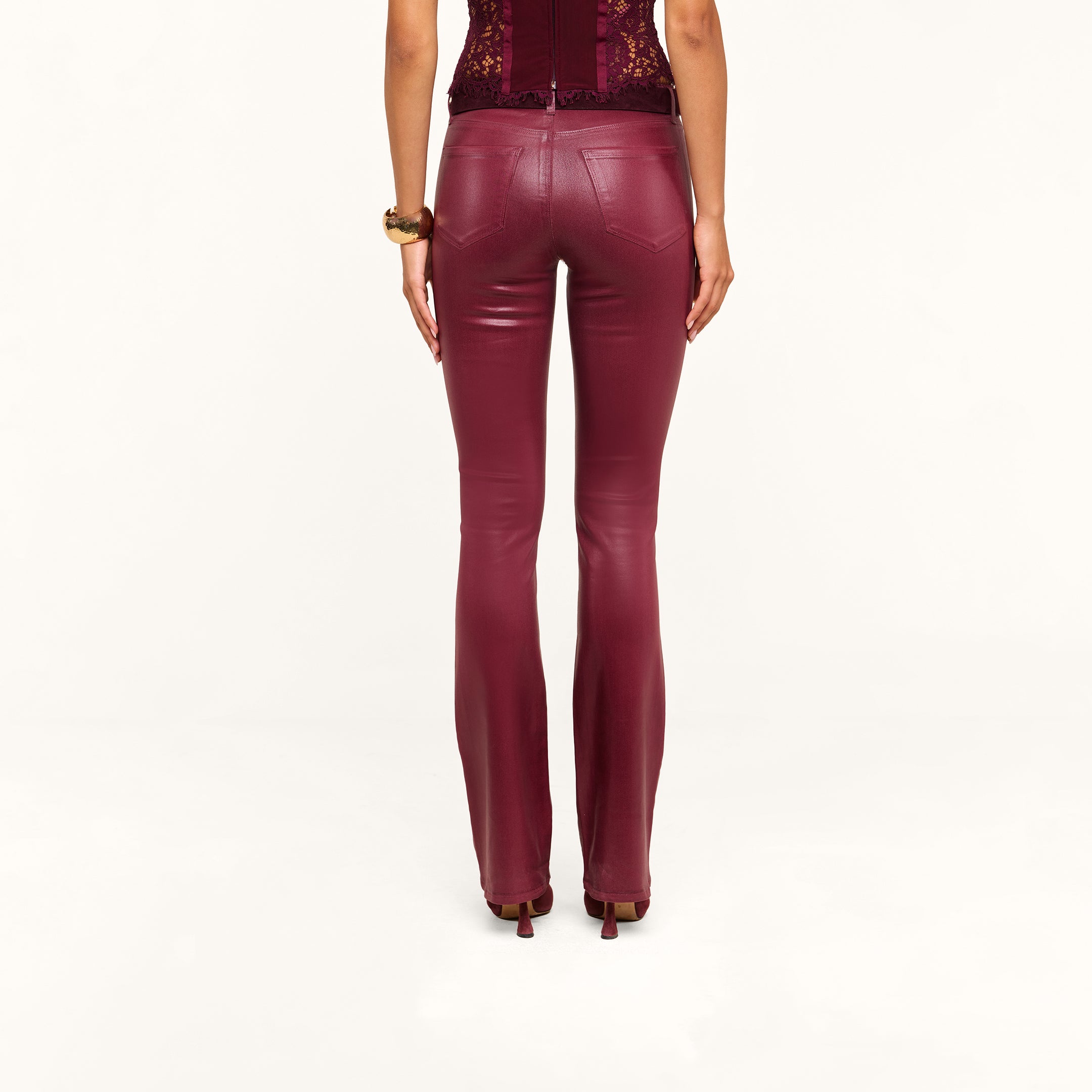 A person wearing the Selma Coated Bootcut Jean in maroon with high heels is standing with their back to the camera against a plain white background.