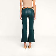 A person stands facing away, wearing the Kendra Coated Cropped Flare Jean in dark teal, paired with a tan sleeveless top and tan high-heeled shoes against a plain white background.
