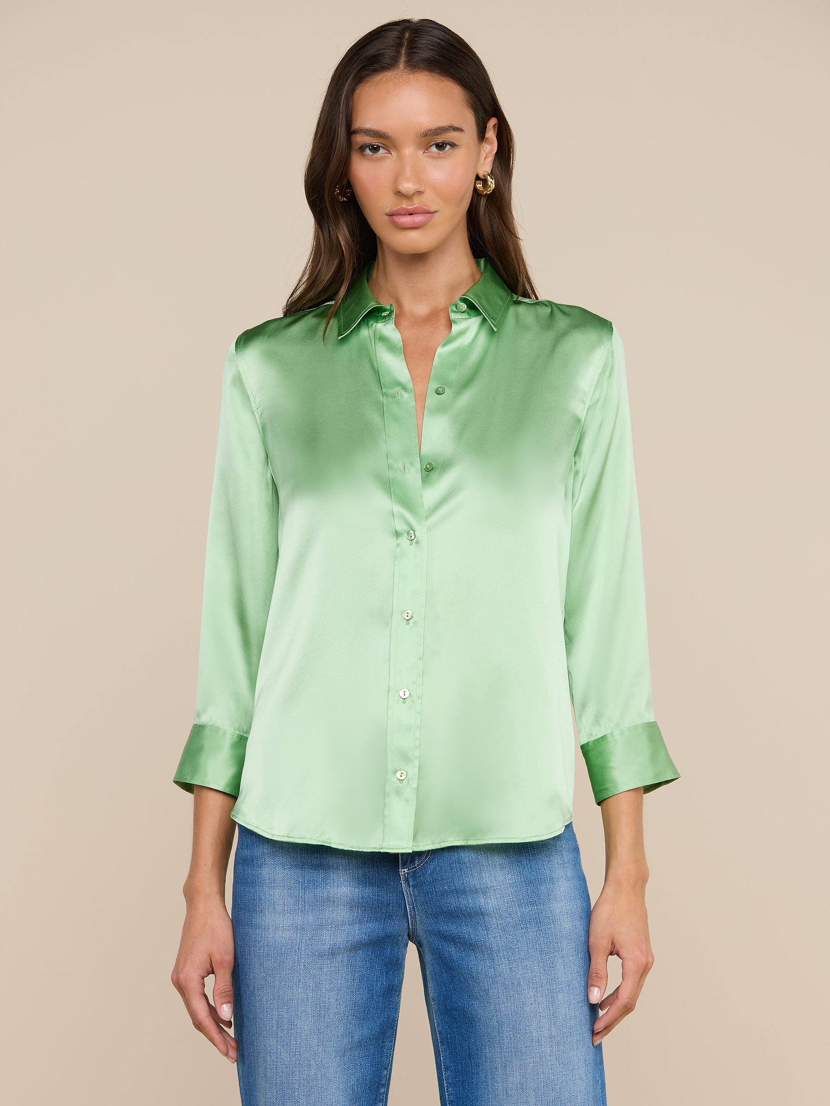 A woman wears a shiny light green Dani Silk Blouse with three-quarter sleeves and blue jeans, standing facing forward against a plain off-white background.