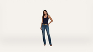 A woman stands facing forward, wearing a navy tank top, blue jeans, and heeled shoes against a plain white background.