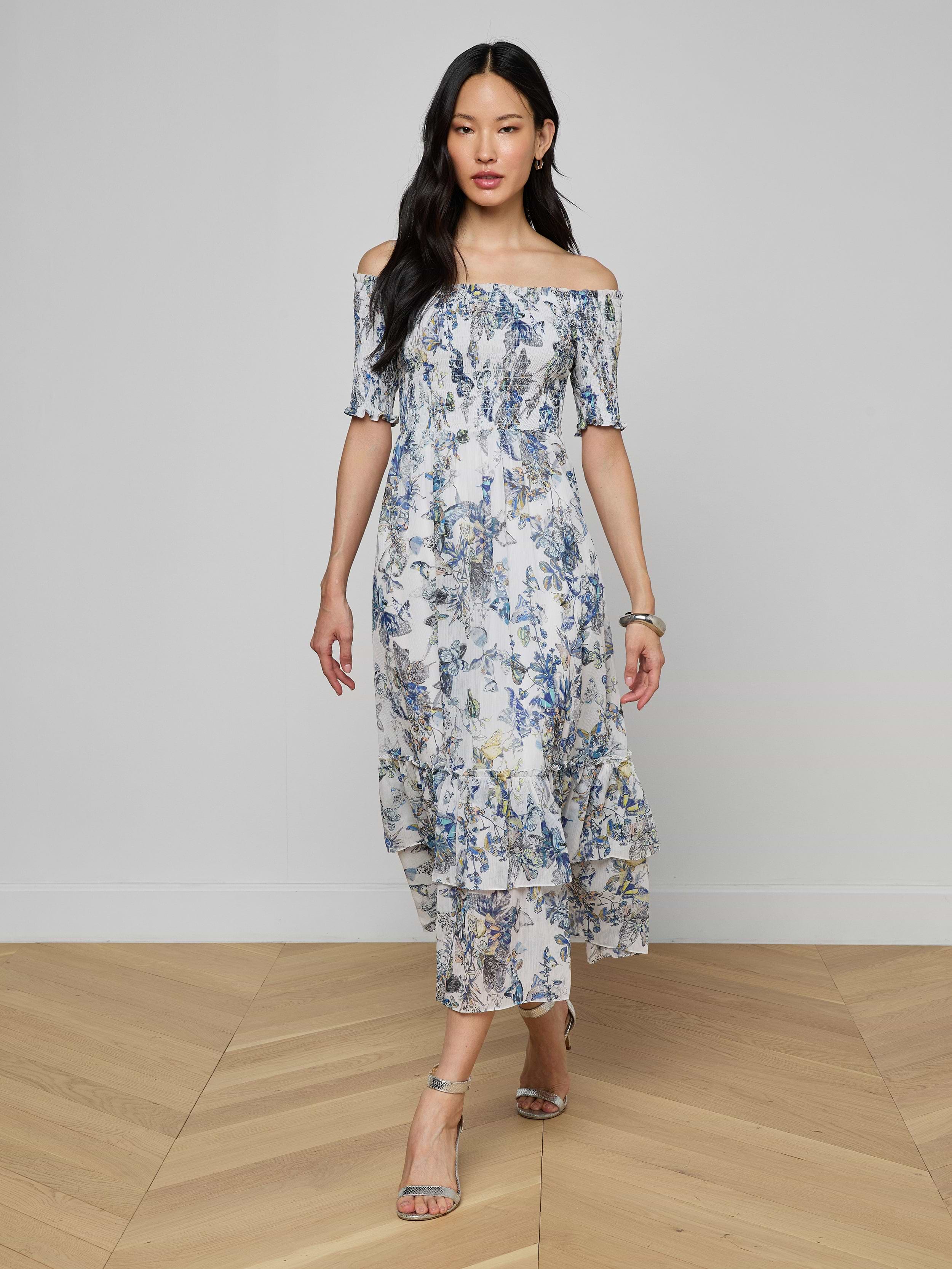 A woman wearing the Oriel Off-Shoulder Dress and sandals stands against a plain light background.