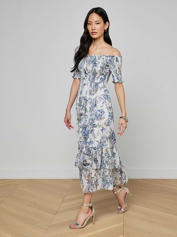 Wearing the Oriel Off-Shoulder Dress and heels, a woman walks confidently against a plain light background.
