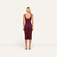 A woman with long blonde hair stands facing away, wearing the fitted Anya Shirred Dress in merlot red and beige heels, against a plain white background.