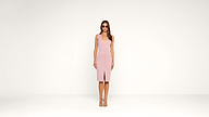 A woman wearing sunglasses and a sleeveless pink dress with a front slit stands facing forward against a plain white background.