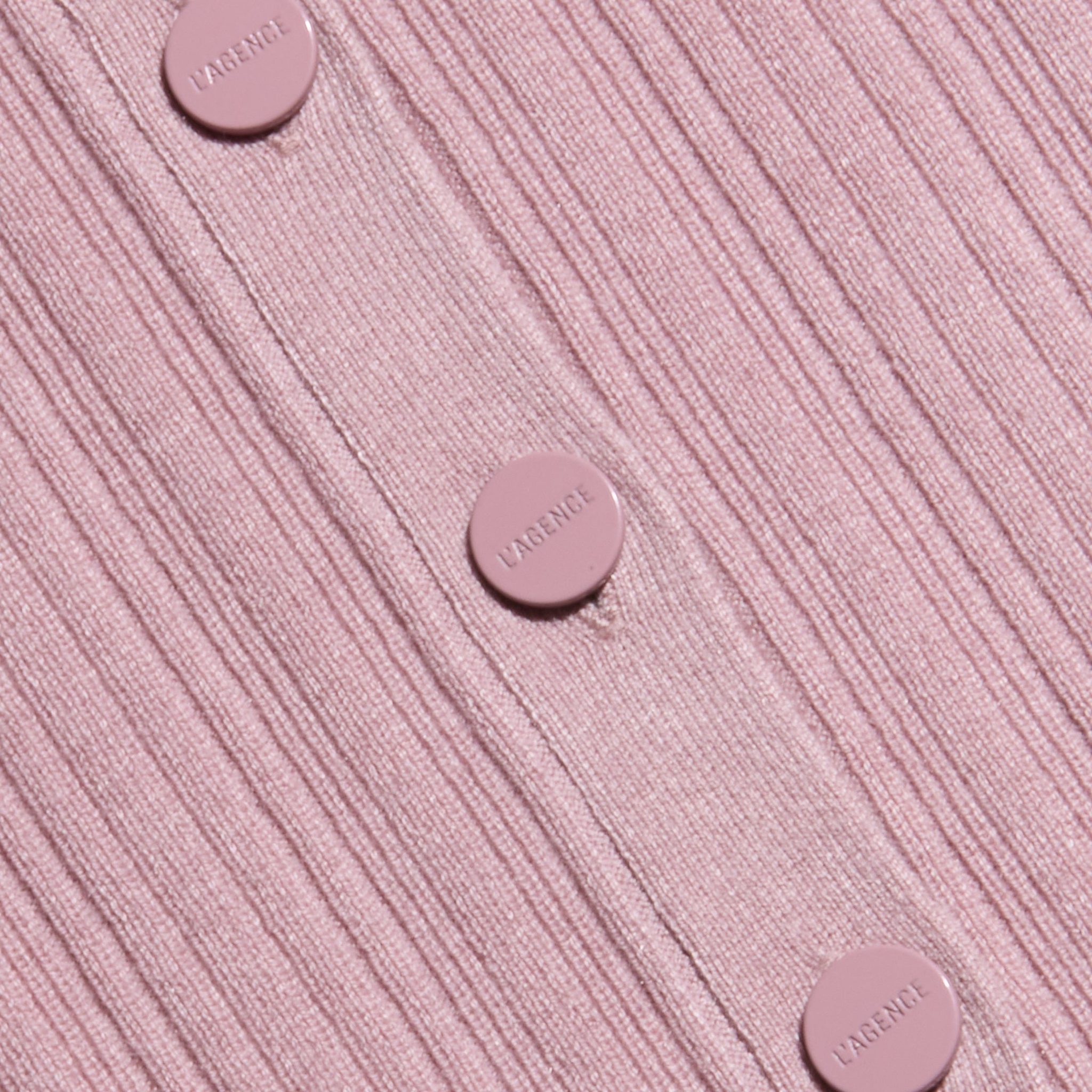 Close-up of the Domino Dress, a ribbed, light pink lightweight knit featuring five matching pink buttons embossed with the word LARENCE, sewn vertically down the garment.