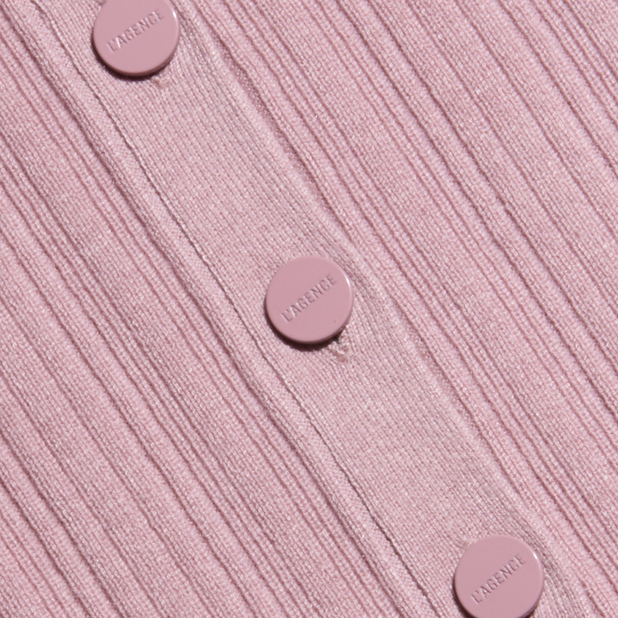 Close-up of the Domino Dress, a ribbed, light pink lightweight knit featuring five matching pink buttons embossed with the word LARENCE, sewn vertically down the garment.
