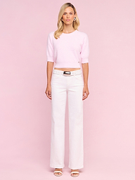 A woman stands facing forward against a plain white background, wearing the Guinevere Cropped Pullover in light pink, paired with white wide-leg belted pants and open-toe heels.