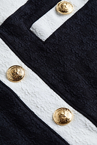 Close-up of the Coco Mini Skirt Cover-Up’s textured bouclé fabric in black and white, accented with gold decorative buttons. The embossed design on the buttons adds a luxurious detail to the garment.