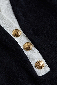 Close-up of three ornate gold buttons on the textured bouclé fabric of the Natalya Collared One-Piece, with a white stripe running underneath. The buttons feature an embossed crest design, highlighting the refined details that define this chic swimsuit.