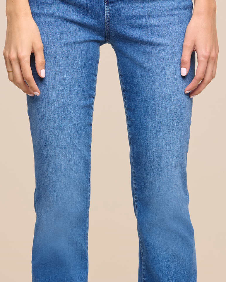 A person wearing light blue denim jeans, shown from the waist to the mid-calf, with hands resting by their sides against a plain beige background.