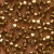 Close-up of multiple shiny, golden oval beads scattered randomly across a brown surface, creating a textured and reflective pattern.
