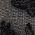 Close-up of a textured fabric with a woven pattern in brown and black colors, featuring some thick black yarns or threads overlapping the surface.