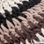 Close-up of a knitted fabric with thick yarn in three colors: white, black, and two shades of brown, arranged in horizontal stripes. The stitches are large and clearly visible, showcasing the texture of the knit.