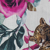A close-up of a floral fabric pattern featuring vibrant pink and purple roses, green leaves, and the face of a brown tiger partially visible on the right side.