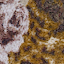 Close-up of a textured fabric with brown, tan, and white patterns, possibly resembling animal print or abstract design. The surface shows a mix of smooth and fuzzy areas.