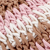 Close-up of crocheted fabric featuring a striped pattern in light pink, white, and brown yarn. The stitches are tightly woven, creating a textured surface.