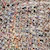 A large crowd of people is gathered close together, seen from above. Most individuals are wearing casual clothing in various colors, creating a dense, textured pattern across the image.