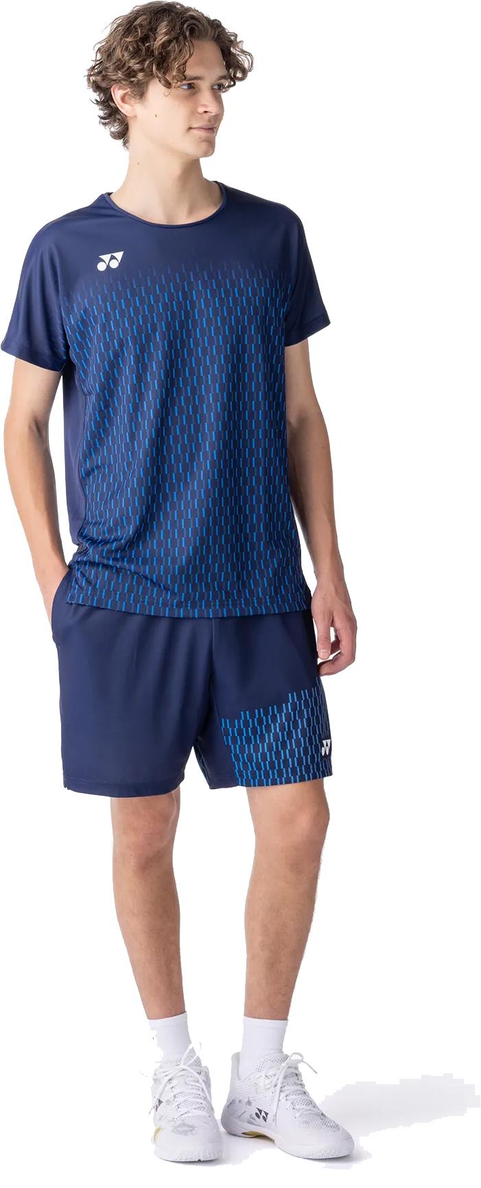 A young man stands hands in pockets, wearing the Yonex 10713EX Crew Neck Men's Badminton T-Shirt in dark navy with light blue patterns, paired with matching shorts and white sneakers—highlighting Yonex’s stylish sportswear and moisture management design.