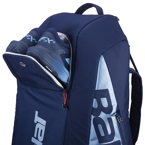 The Babolat RH6 Pure Drive Gen11 in navy blue, made from recycled polyester, shows two blue sports shoes inside its partially open pocket. It features a large zipper and white brand lettering on the side, resembling a sleek badminton racket bag.