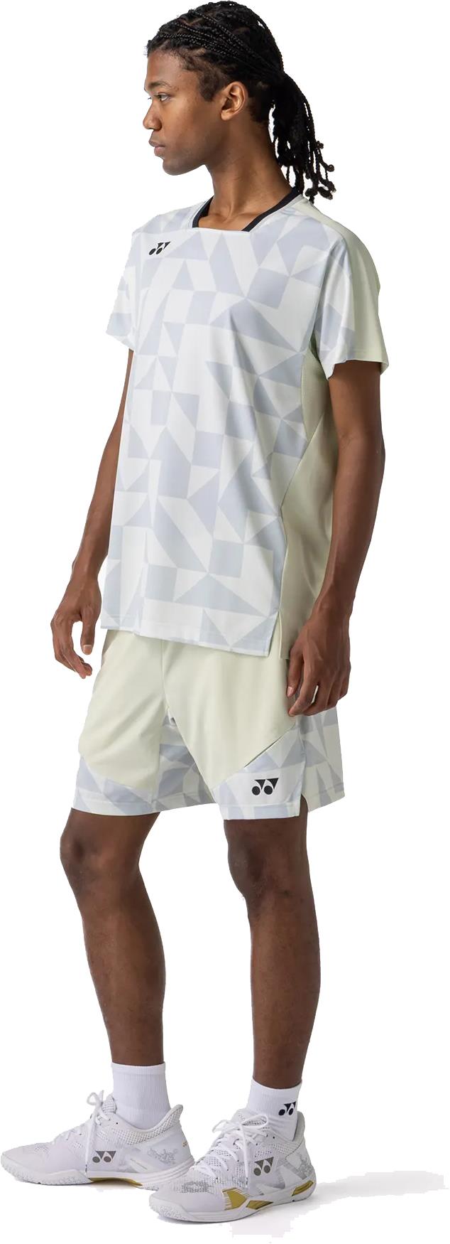 A person with long braided hair wears the Yonex 10712YX Crew Neck Men's Badminton T-Shirt in Champagne, matching shorts, white socks, and white athletic shoes while standing and looking left against a white background.