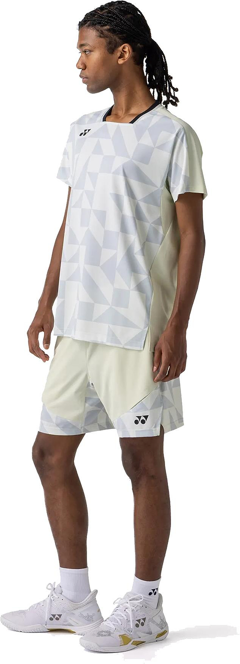 A person with long braided hair wears the Yonex 10712YX Crew Neck Men's Badminton T-Shirt in Champagne, matching shorts, white socks, and white athletic shoes while standing and looking left against a white background.