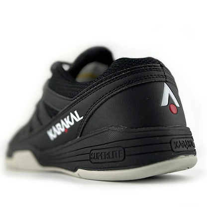 Close-up of a Karakal KF Pro Lite Badminton Shoe in black, showcasing the Karakal logo with a red dot on the side. The heel displays "Superlite" to enhance lateral stability, while the cushioned sole features textured details and incorporates a shock-absorbing gel insole for superior comfort.