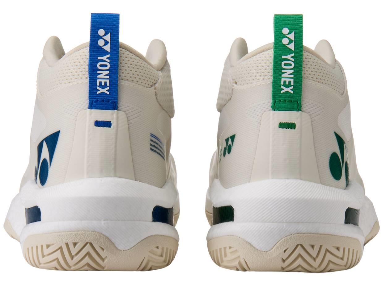 Rear view of Yonex Power Cushion GRPHT THRTTL Concept men's badminton shoes in off-white; left shoe with blue heel tab, right with green. Both feature Yonex logos, patterns, and advanced Power Graphite technology.