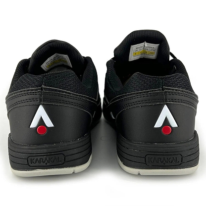The image showcases the rear view of Karakal KF Pro Lite Badminton Shoes - New Black, highlighting black uppers paired with gray soles. The heels feature a white and red triangular logo, along with "Karakal" embossed on them, ensuring lateral stability and incorporating an advanced shock-absorbing gel insole to boost performance.