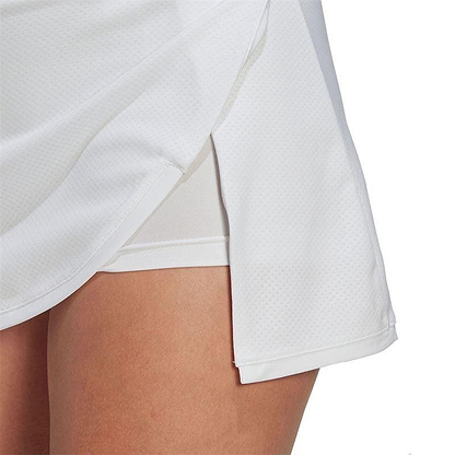 Close-up of an individual wearing a white ADIDAS Women's Club Badminton Skirt. The skirt includes a side slit that reveals part of the shorts underneath. Made from lightweight, textured fabric and enhanced with AEROREADY technology, it ensures maximum comfort and breathability during play.